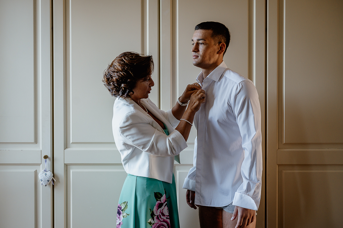 matrimonio a Chieri, preparazione dello sposo, mamma dello sposo che abbottona la camicia dello sposo