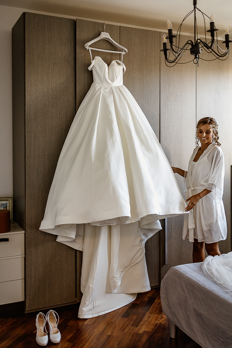 matrimonio a Chieri, preparazione della sposa, sposa che tocca il suo abito appeso all'armadio