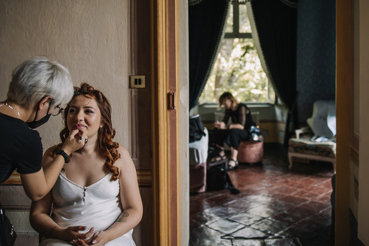 Matrimonio al Castello Canalis di Cumiana(TO). La make-up artist Gloria Corradino trucca le labbra della sposa. Sullo sfondo nella camera da letto si ivede la parrucchiera che attende di pettinare la sposa