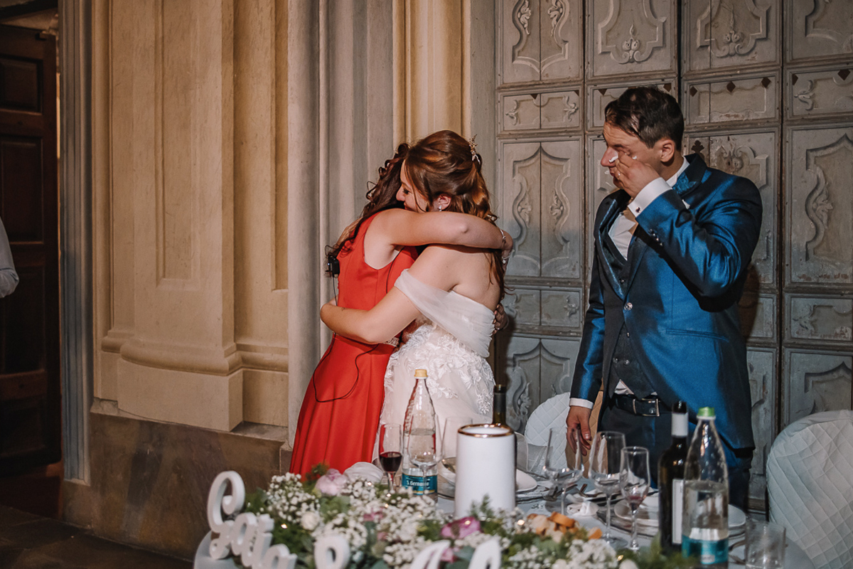 Matrimonio al Castello Canalis di Cumiana(TO). Cena.Sposa che abbraccia la testimone. Sposo che si asciuga una lacrima