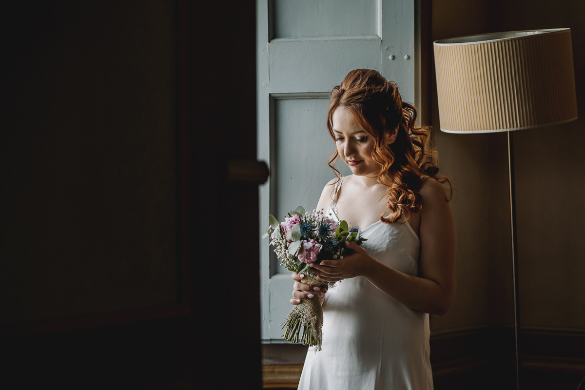 Matrimonio al Castello Canalis di Cumiana(TO). Sposa che guarda il suo bouquet davanti alla finestra