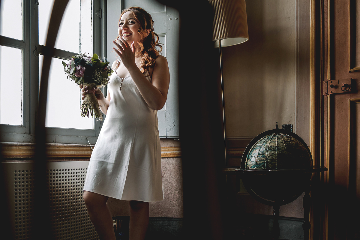 Matrimonio al Castello Canalis di Cumiana(TO). Sposa davanti alla finestra che ride con il bouquet in mano