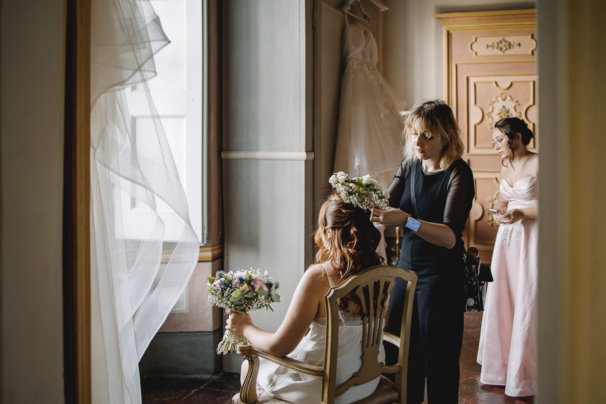 Matrimonio al Castello Canalis di Cumiana(TO). Parrucchiera che pone una coroncina di fiori freschi sul capo della sposa