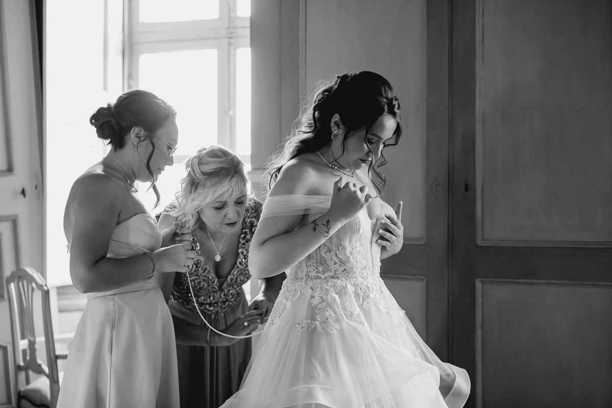 Matrimonio al Castello Canalis di Cumiana(TO). Mamma e sorella che aiutano la sposa a chiudere l'abito