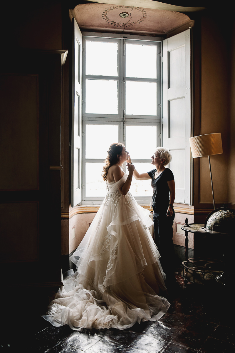 Matrimonio al Castello Canalis di Cumiana(TO). Truccatrice che fa gli ultimi ritrocchi al trucco della sposa davanti alla finestra.