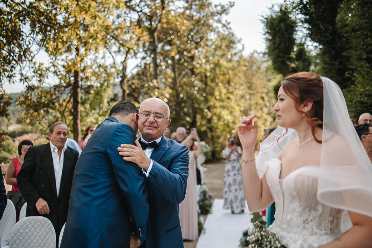 Matrimonio al Castello Canalis di Cumiana(TO). Cerimonia. Padre della sposa che abbraccia lo sposo commosso. anche la sposa guarda commossa.