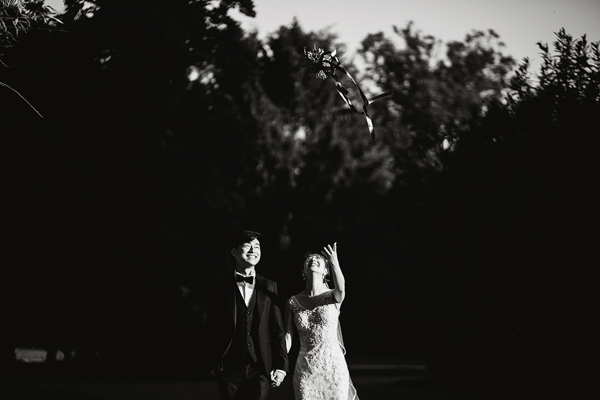 Castello di Collegno, matrimonio cinese. Cerimonia occidentale. Fotografia di coppia. Sposi che camminano e sposa che lancia il bouquet. Bianco e nero.