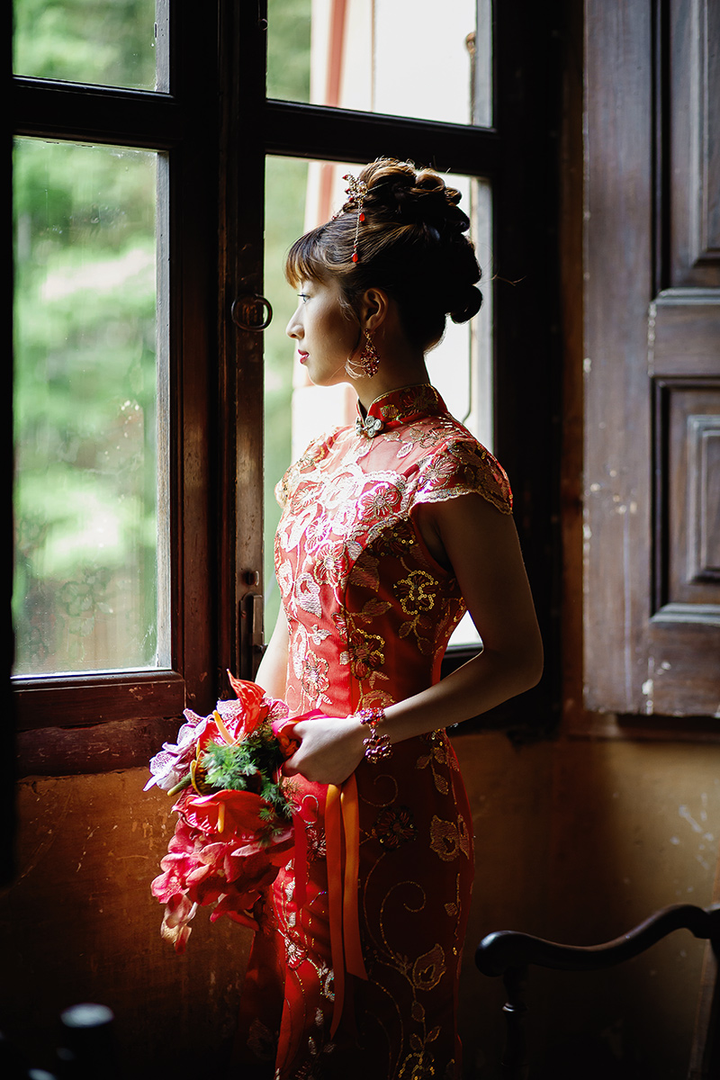 Castello di Collegno, matrimonio cinese. Cerimonia tradizionale. Preparazione della sposa. Ritratto della sposa con l'abito tradizionale rosso ed oro alla finestra.