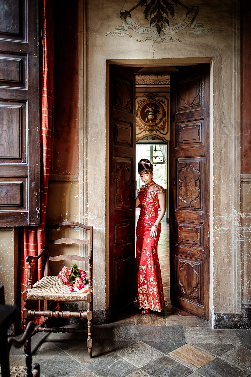 Castello di Collegno, matrimonio cinese. Cerimonia tradizionale. Preparazione della sposa. Ritratto della sposa con l'abito tradizionale rosso ed oro nel vano di una porta antica.