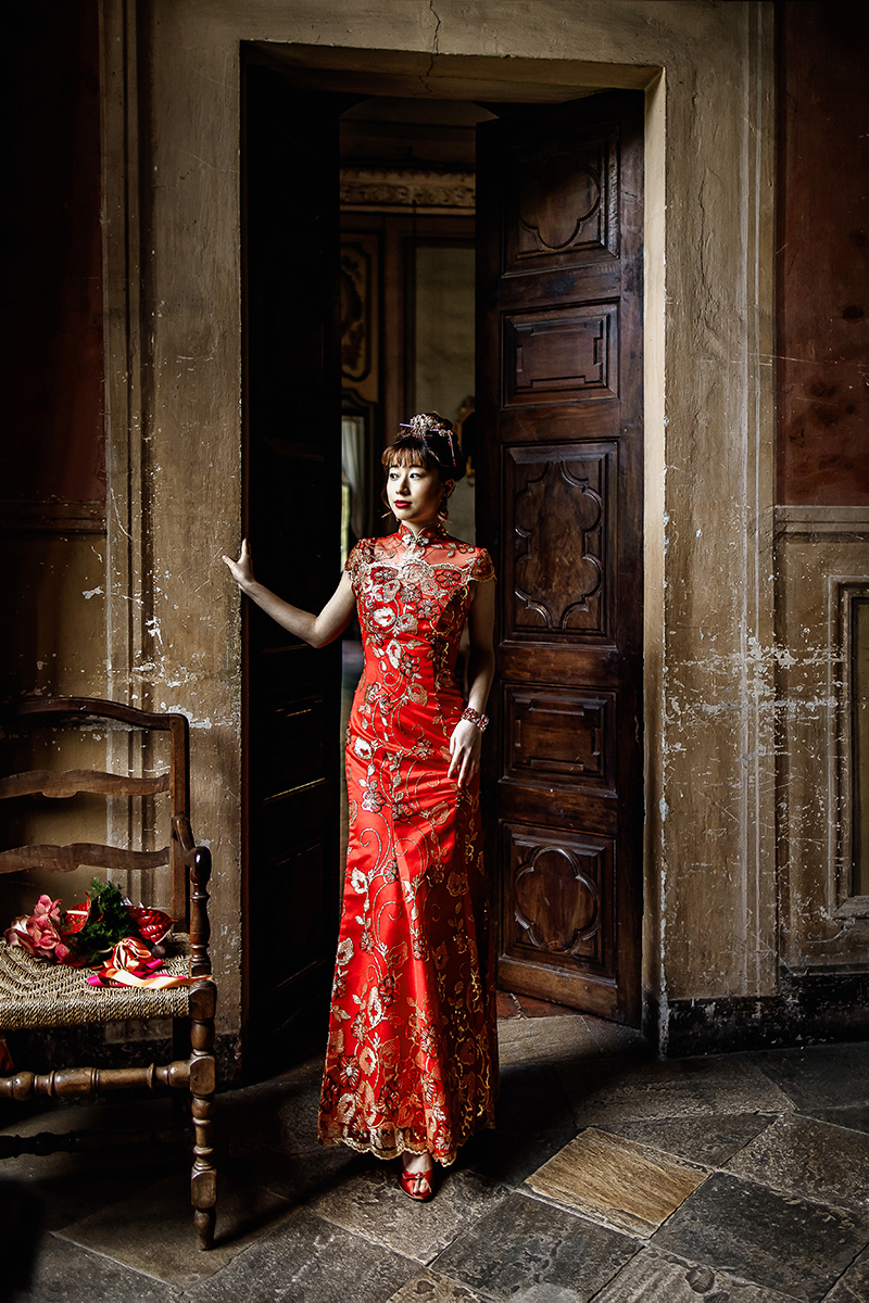 Castello di Collegno, matrimonio cinese. Cerimonia tradizionale. Preparazione della sposa. Ritratto della sposa con l'abito tradizionale rosso ed oro appoggiata allo stipite di una porta antica.