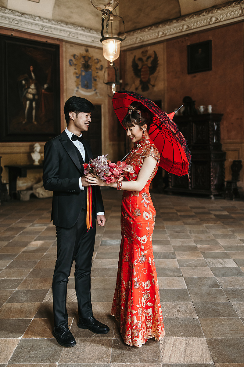 Castello di Collegno, matrimonio cinese. Cerimonia tradizionale. Preparazione della sposa. Ritratto degli sposi. Sposo porge il bouquet alla sposa che ha un ombrellino di seta rosso.