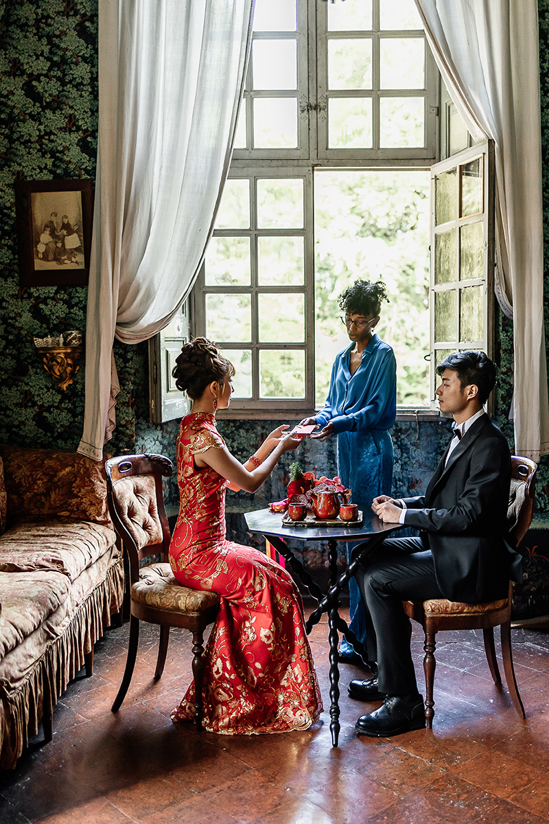 Castello di Collegno, matrimonio cinese. Cerimonia del tè tradizionale. la cerimoniera consegna la tradizionale busta rossa, 传统婚礼红包, alla sposa.. Salottino cinese del castello. Sposi seduti al tavolino da tè. La cerimoniera consegna la tradizionale busta rossa.
