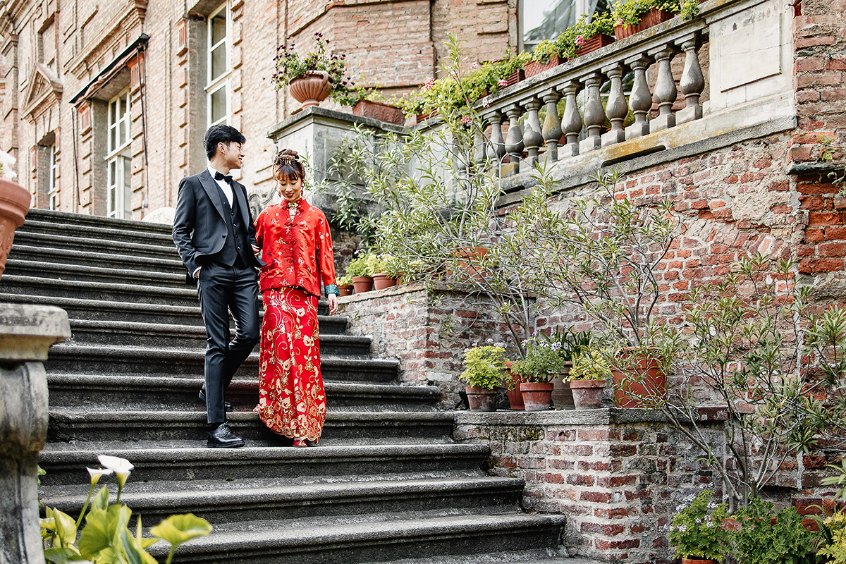 Castello di Collegno, matrimonio cinese. Cerimonia tradizionale. Sessione fotografica di coppia. sposa indossa una giacca tradizionale cinese di seta rossa ricamata. Sposi scendono lo scalone esterno del castello.