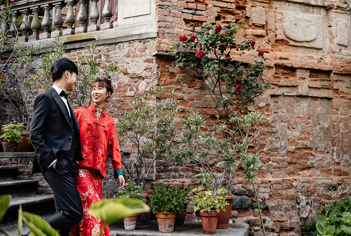 Castello di Collegno, matrimonio cinese. Cerimonia tradizionale. Sessione fotografica di coppia. sposa indossa una giacca tradizionale cinese di seta rossa ricamata. Sposi scendono lo scalone esterno del castello. e si guardano.