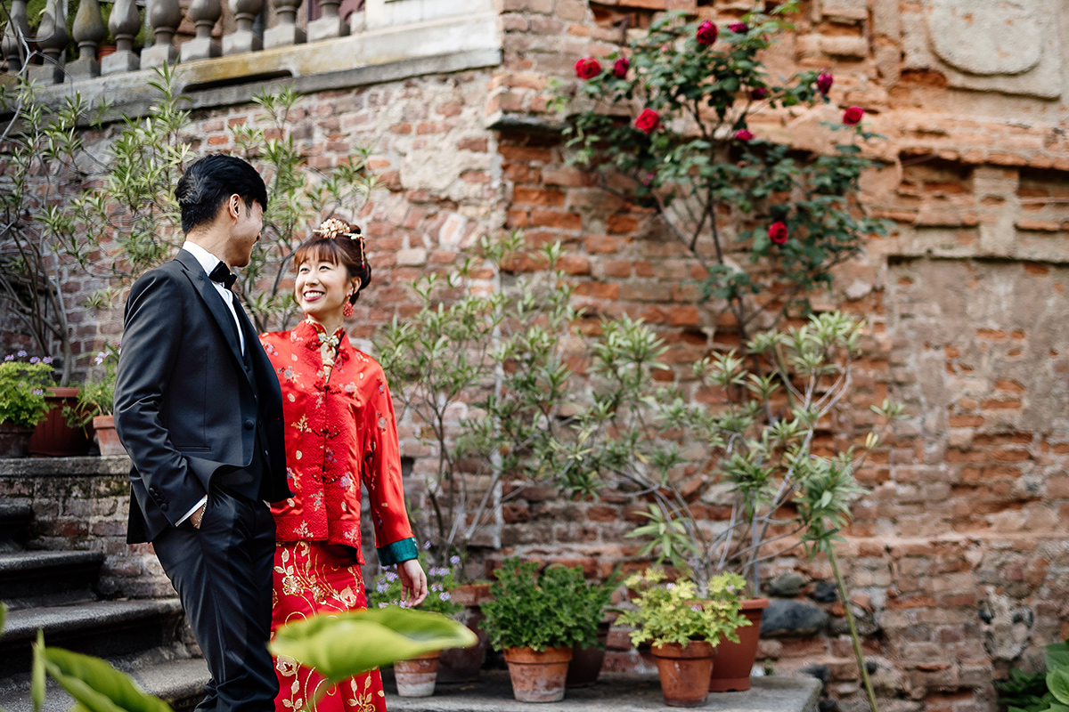 Castello di Collegno, matrimonio cinese. Cerimonia tradizionale. Sessione fotografica di coppia. sposa indossa una giacca tradizionale cinese di seta rossa ricamata. Sposi scendono lo scalone esterno del castello.