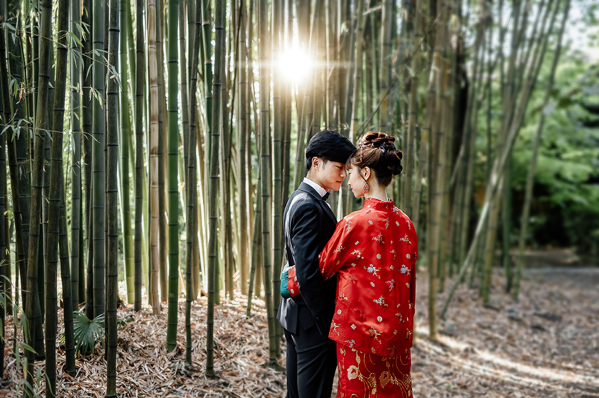 Castello di Collegno, matrimonio cinese. Cerimonia tradizionale. Sessione fotografica di coppia. sposa indossa una giacca tradizionale cinese di seta rossa ricamata. Ritratto intimo degli sposi nel bosco di bambù con il sole che fa capolino fra gli steli dei bambù.