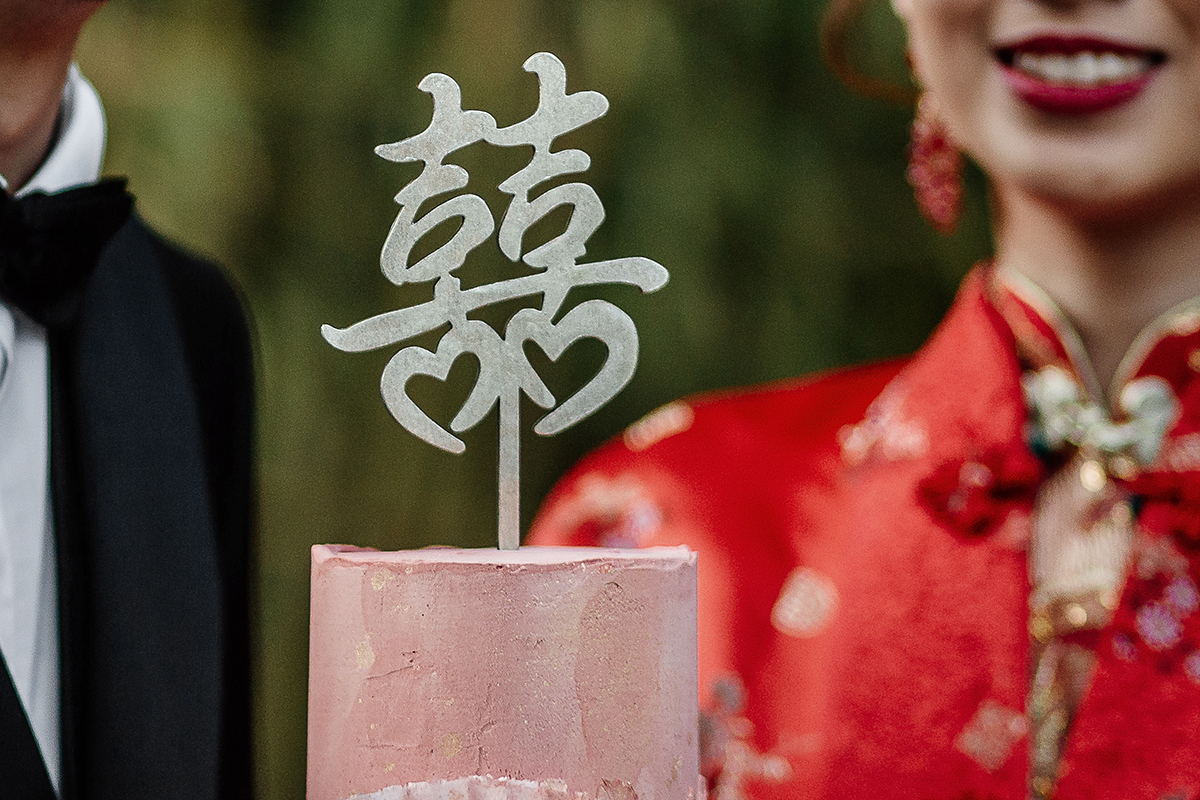 Castello di Collegno, matrimonio cinese. Cerimonia tradizionale. Sessione fotografica di coppia. sposa indossa una giacca tradizionale cinese di seta rossa ricamata.Sposi camminano nel bosco dei bambù con la torta che ha per topper il carattere cinese della doppia felicità"囍"