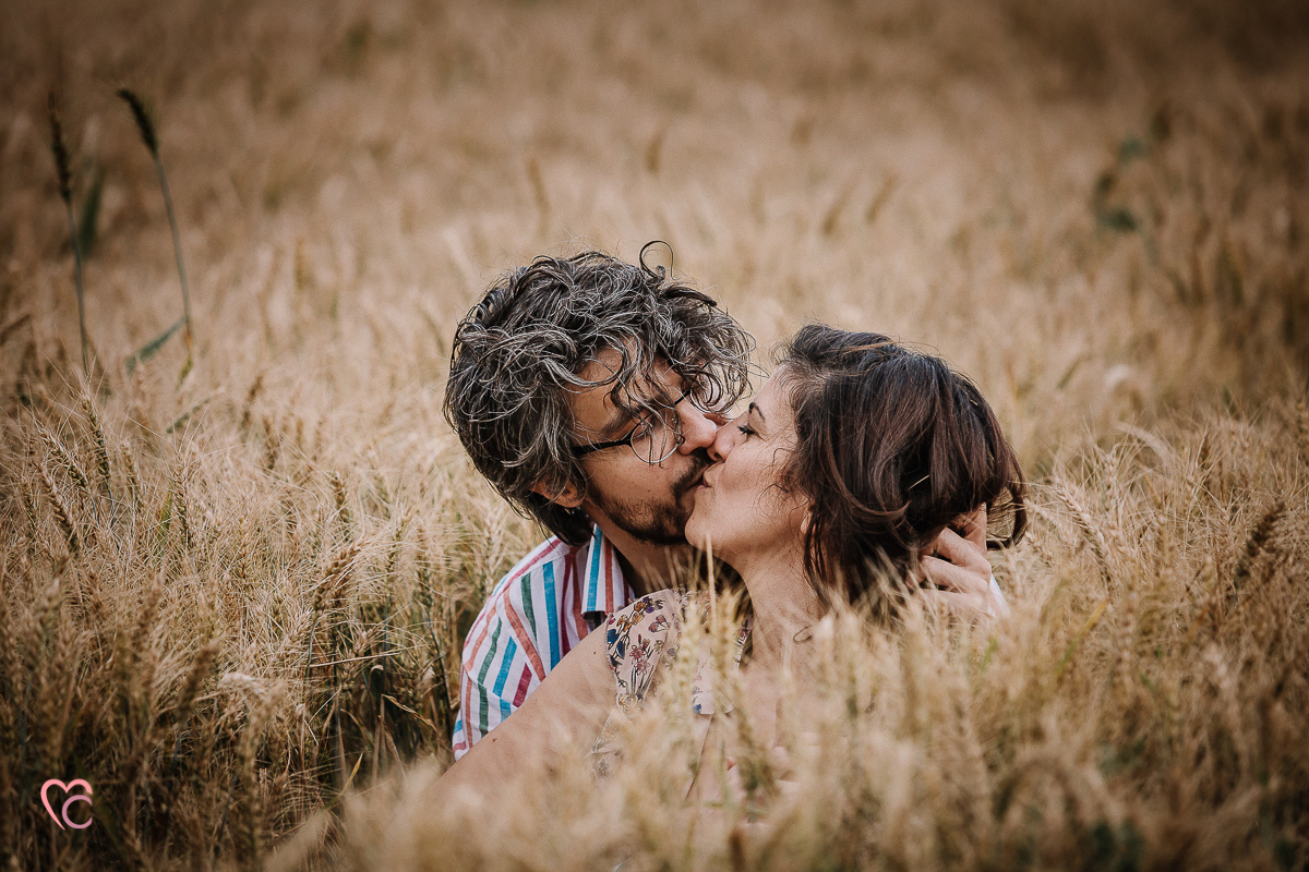 Fotografia di coppia in collina a Chieri. Daniela e Gianluca seduti nel campo di grano. si baciano