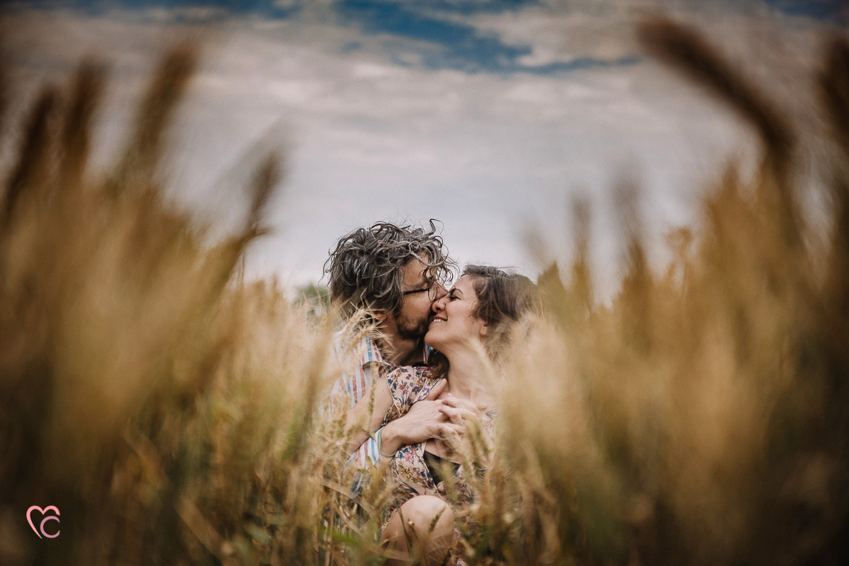 Fotografia di coppia in collina a Chieri. Daniela e Gianluca seduti nel campo di grano. si baciano