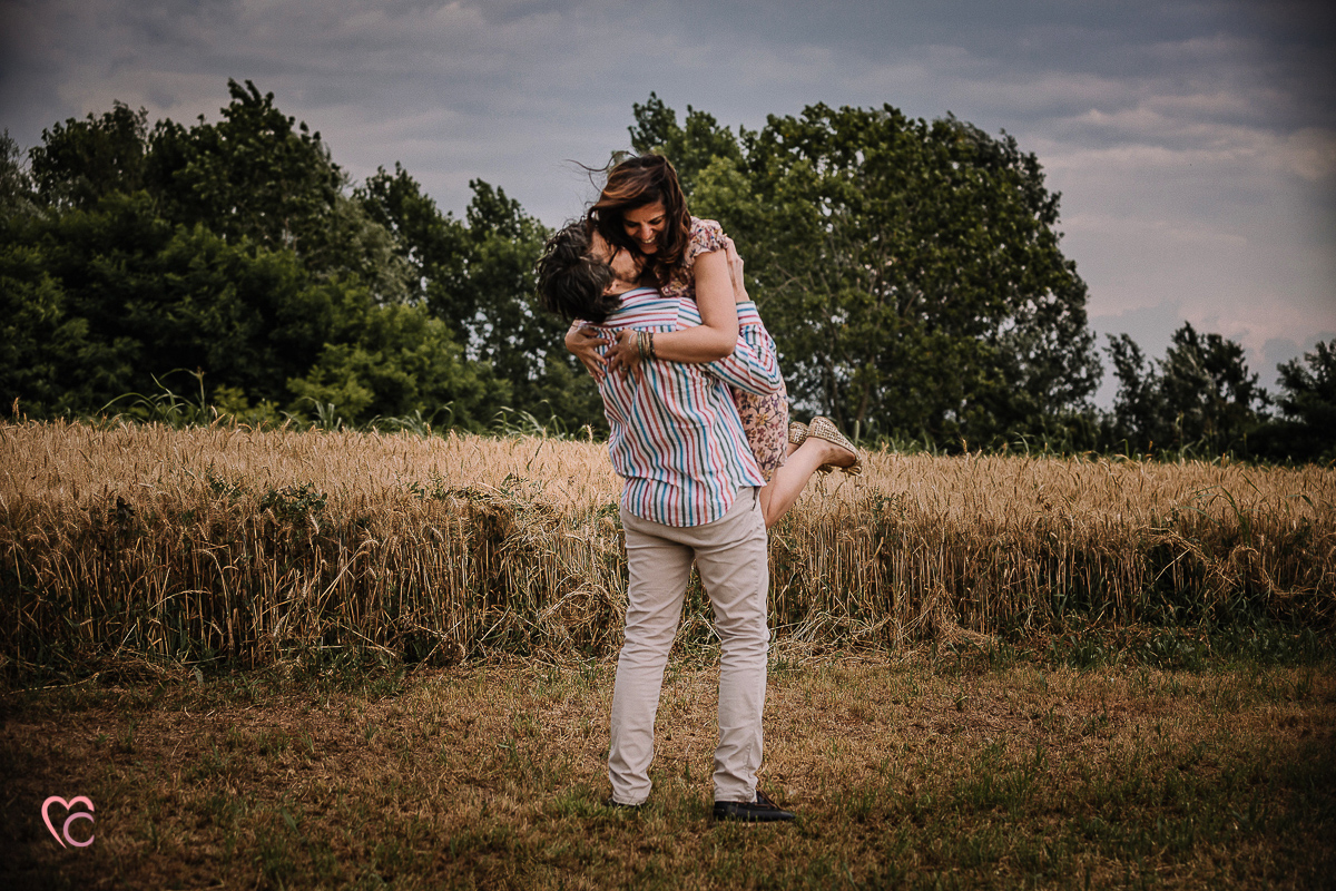 Fotografia di coppia in collina a Chieri. Daniela e Gianluca nel campo di grano Gianluca prende in braccio Daniela