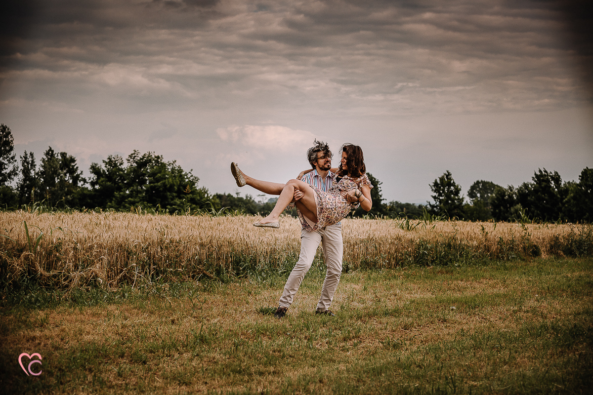 Fotografia di coppia in collina a Chieri. Daniela e Gianluca nel campo di grano Gianluca prende in braccio Daniela