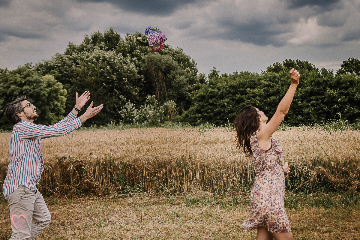 Fotografia di coppia in collina a Chieri. Daniela e Gianluca giocano. Daniela lancia un bouquet di ortensie a Gianluca.