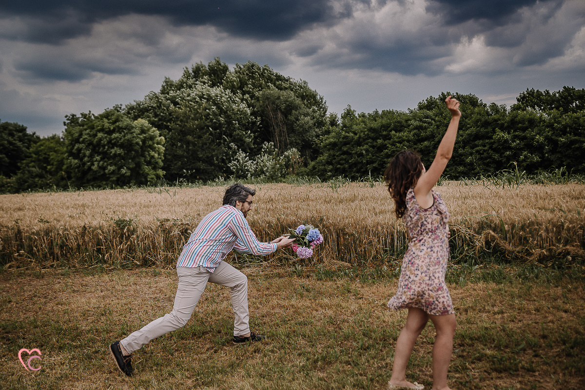 Fotografia di coppia in collina a Chieri. Daniela e Gianluca giocano. Daniela lancia un bouquet di ortensie a Gianluca.
