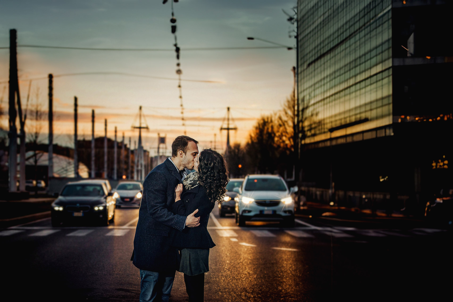 Engagement a Torino nella stazione di Porta Susa. Coppia si bacia sulle strisce pedonali di corso Inghilterra al tramonto davanti alle auto ferme con i fari accesi e davanti al grattacielo Intesa San Paolo.