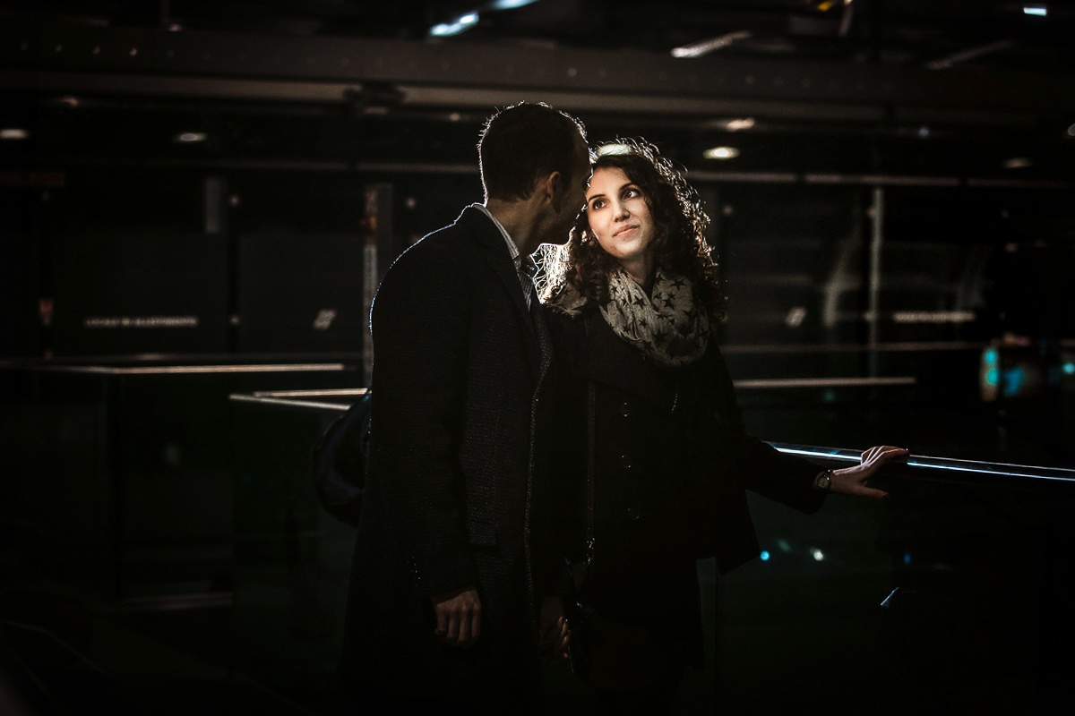 Engagement a Torino nella stazione di Porta Susa. Coppia ll'interno della stazione sulla scala mobile. Ritratto con flash esterno.