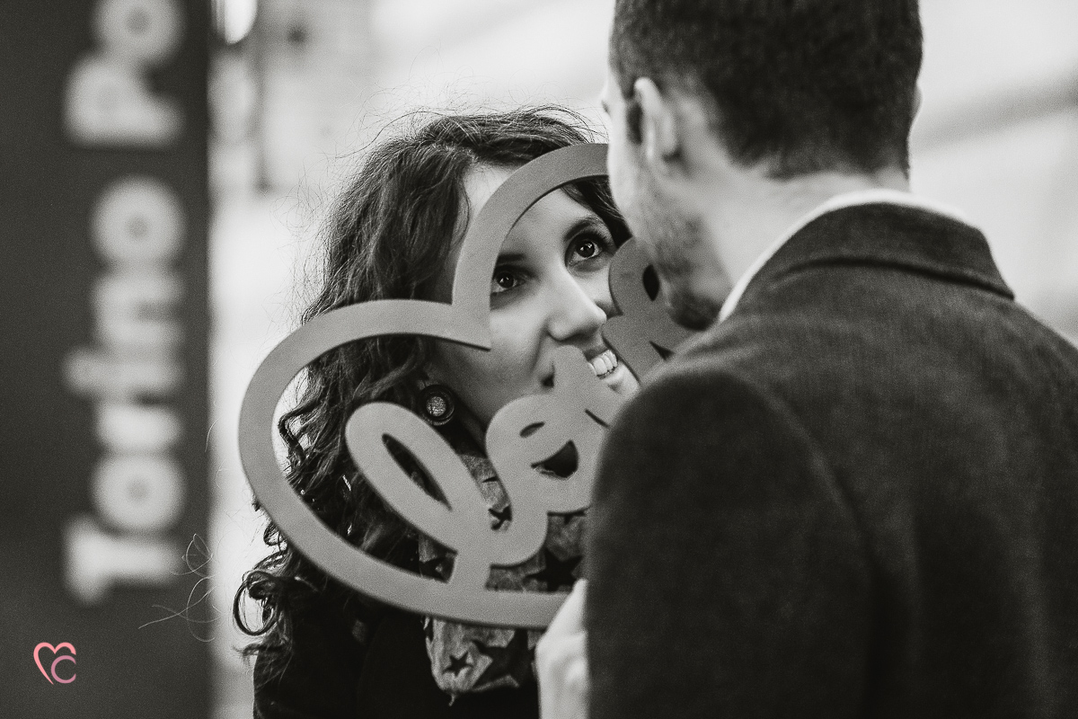 Engagement a Torino nella stazione di Porta Susa. La coppia si tiene in mano un cuore rosso con la scritta love Bianco e nero.