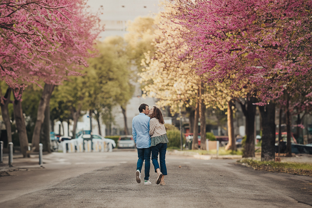 Servizio fotografico di coppia alla Crocetta di Torino.. Fioritura dei ciliegi rosa. Hanami. Coppia si bacia camminando.