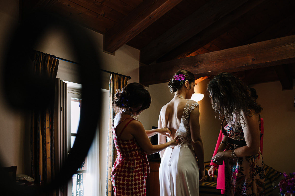 Castello Rosso di Costigliole di Saluzzo. Destination wedding. Vestizione della sposa. Testimone abbottona l'abito.