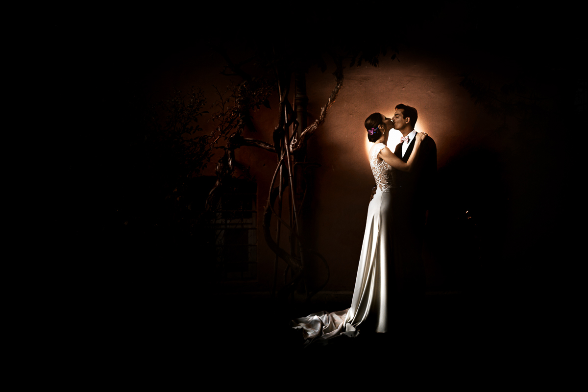 Castello Rosso di Costigliole di Saluzzo. Destination wedding. Sessione di coppia al tramonto. Bacio degli sposi davanti ad una parrete color terracotta. Flash off camera dietro gli sposi puntato contro il muro.