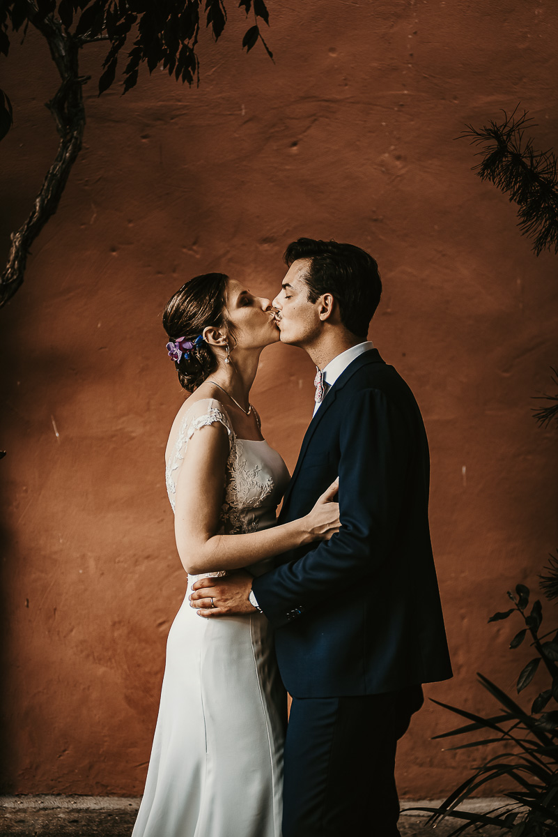 Castello Rosso di Costigliole di Saluzzo. Destination wedding. Sessione di coppia al tramonto. Bacio degli sposi davanti ad una parrete color terracotta. Flash off camera dietro gli sposi