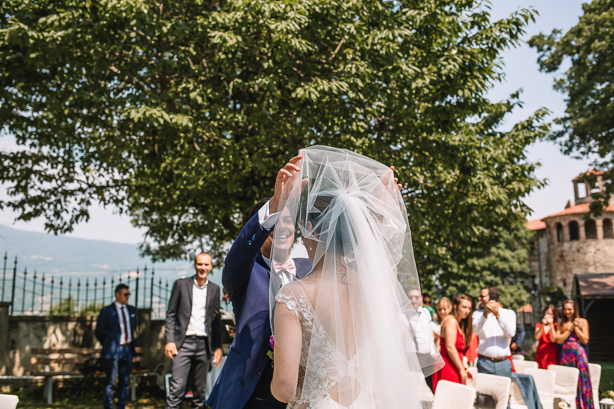 Castello Rosso di Costigliole di Saluzzo. Destination wedding. Cerimonia. Sposo solleva il velo alla sposa.