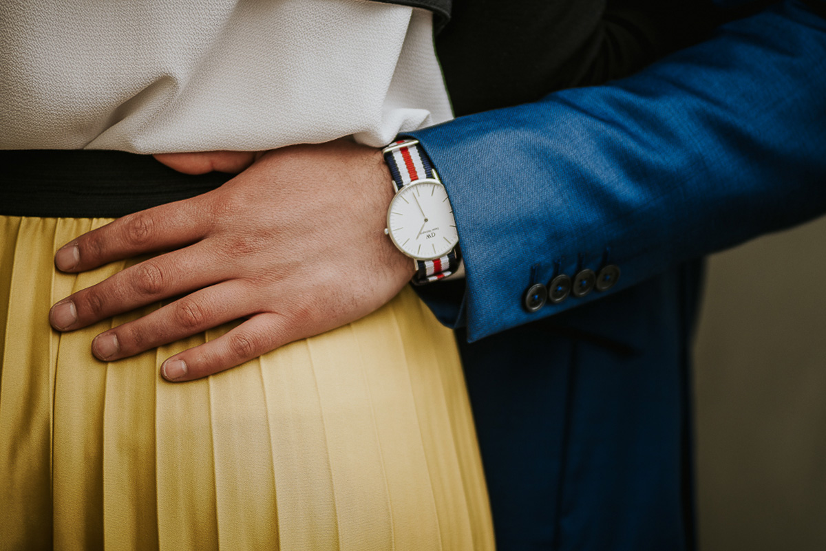 Engagement a Torino, in piazza Vittorio Veneto a Torino di Sara e Gabriel. Coppia sotto un arco dei portici dettaglio della mano e dell'orologio di Gabriel con il cinturino con la bandiera francese