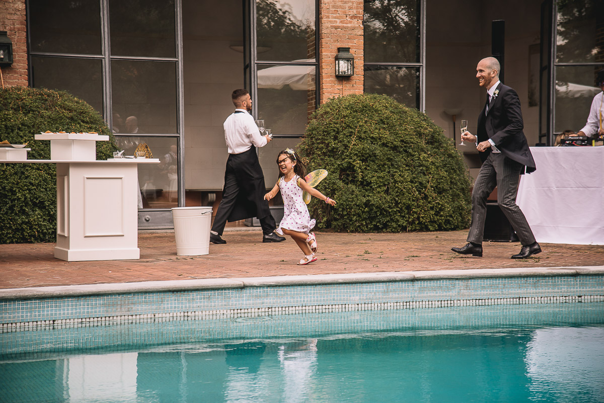 Matrimonio nella Villa dei Marchesi di Moncrivello. Servizio di coppia.Aperitivo.Bimba che corre a bordo piscina con un paio di ali.
