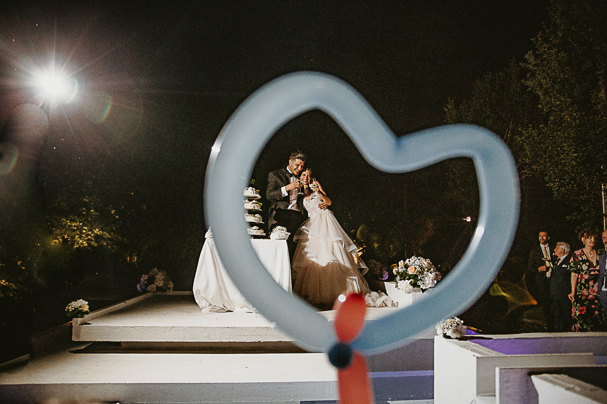 Matrimonio alla Tenuta La Cascinetta di Buriasco. Ricevimento. Taglio della torta. Sposi fotografati attraverso un palloncino a forma di cuore