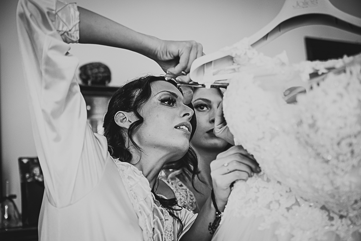 Matrimonio in centro a Torino. Preparazione della sposa. Sposa che taglia i nastrini che sostengono l'abito.