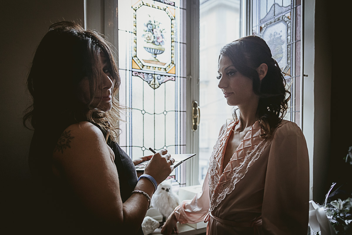 Matrimonio in centro a Torino. Preparazione della sposa. Trucco della sposa di fronte alla finestra