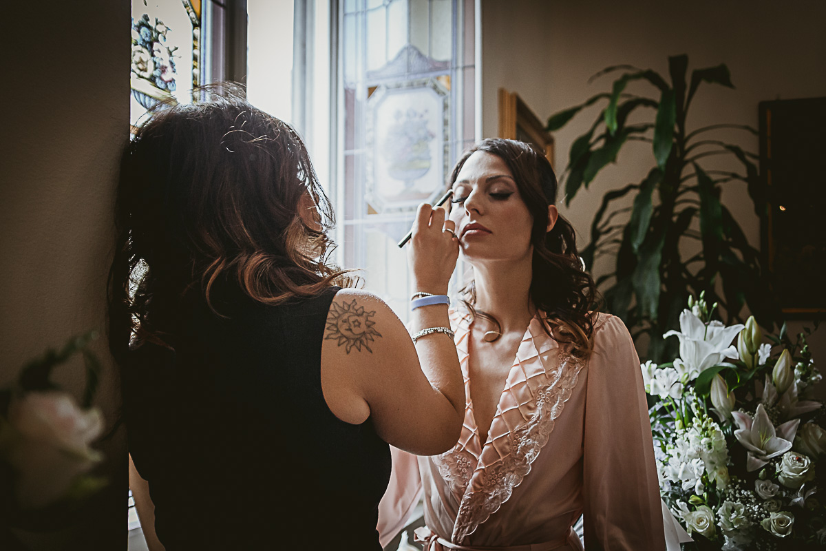 Matrimonio in centro a Torino. Preparazione della sposa.Trucco della sposa di fronte alla finestra