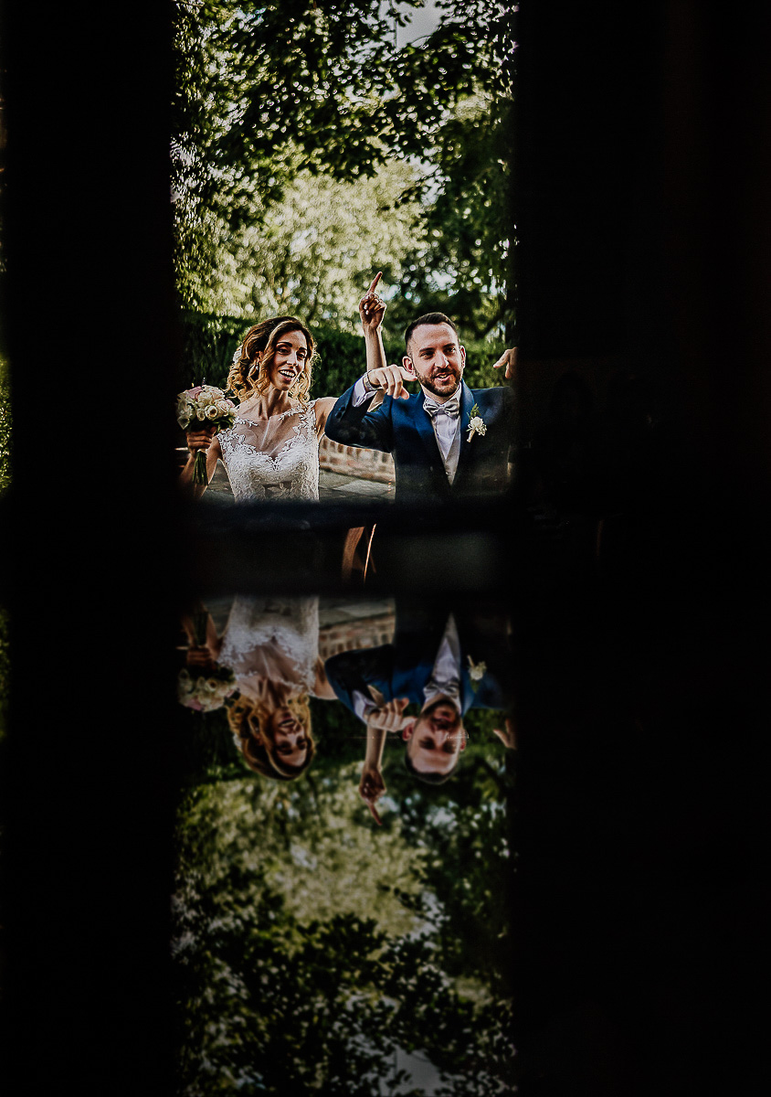 Matrimonio al castello di Cortanze. Aperitivo.Sposi che stanno per entrare in sala riflessi nella porta a vetri.