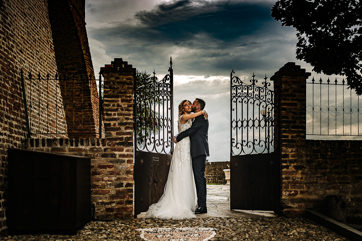 Matrimonio al castello di Cortanze. Sessione di coppia. Sposi che si abbracciano vicino ad un cancello con cielo drammatico