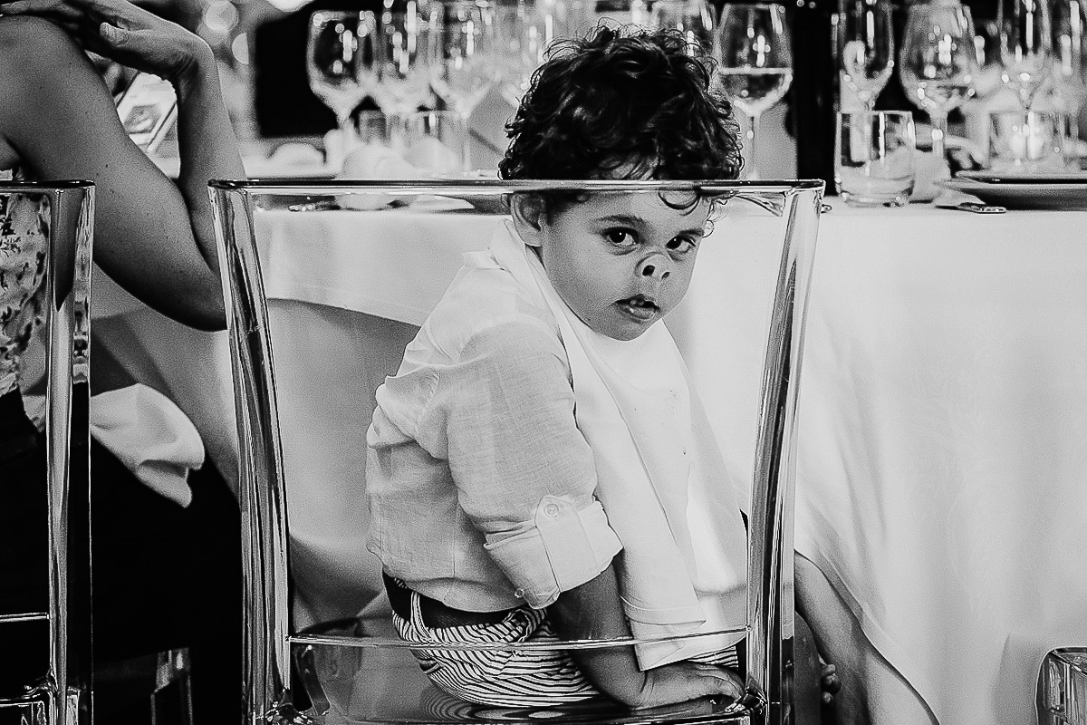 Matrimonio al castello di Cortanze. Ricevimento. Piccolo invitato che schiaccia il viso contro una sedia di Kartell di plastica trasparente e sembra un maialino.