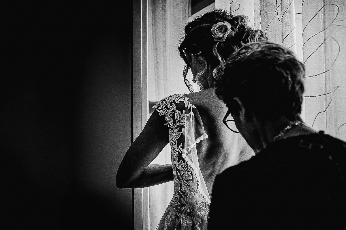 Matrimonio a Torino, preparazione della sposa.Madre che abbottona l'abito della sposa in bianco e nero.