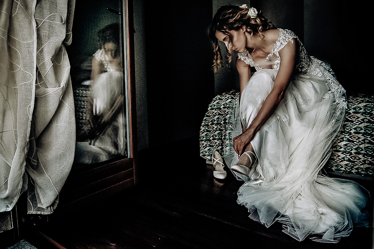 Matrimonio a Torino, preparazione della sposa.Sposa che si mette le scarpe riflessa nella porta-finestra.