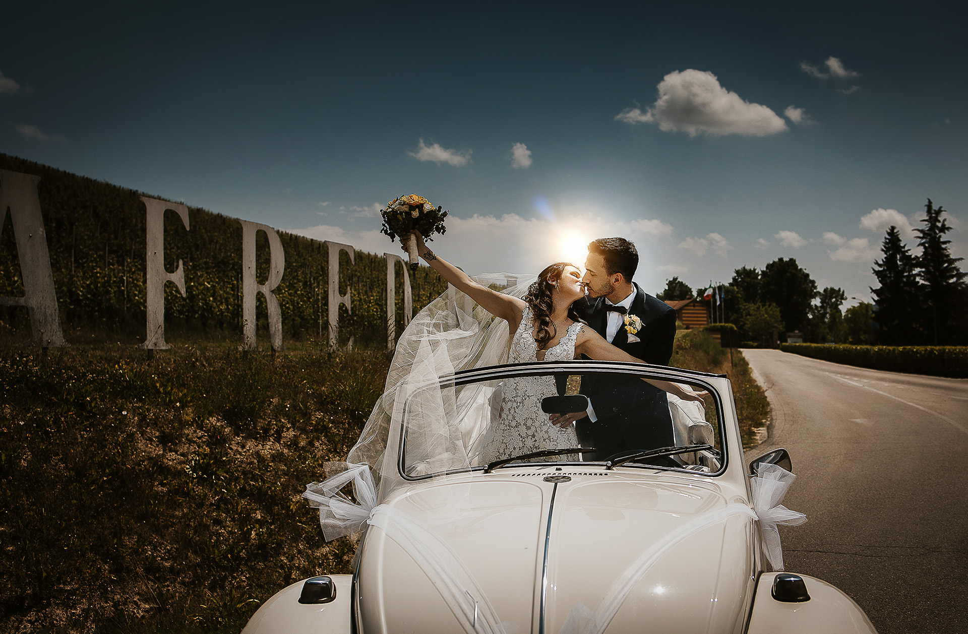 Tenuta Fontanfredda, Guidoristorante. Villa reale.Sessione fotografica degli sposi tra le vigne. Arrivo nella tenuta. Sposi in pedi in auto che si baciano. Con il sole dietro di loro.