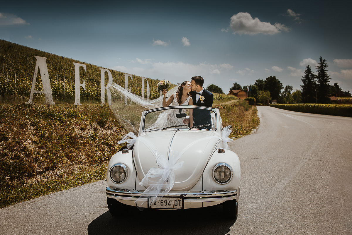 Tenuta Fontanfredda, bacio degli sposi in piedi in auto, velo che vola