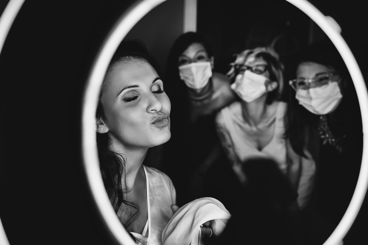 Matrimonio a Torino. Preparazione della sposa. Sposa illuminata da una ring light e amiche che le mandano un bacio