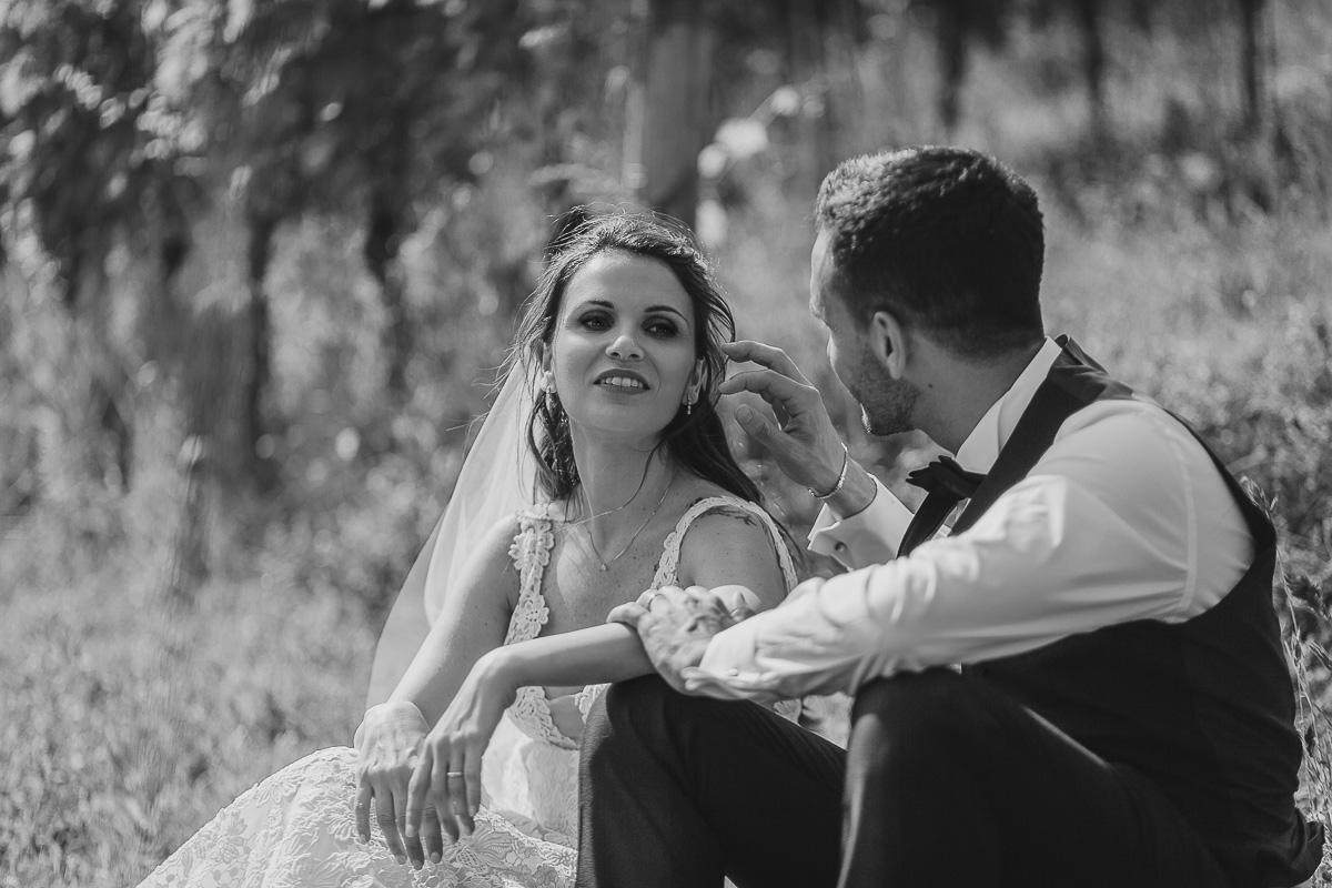 Tenuta Fontanfredda, Guidoristorante. Villa reale.Sessione fotografica degli sposi tra le vigne. Sposi seduti per terra. Sposo scosta i capelli dal viso della sposa.